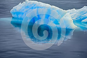 Blue growler (piece of iceberg) with reflection in calm water