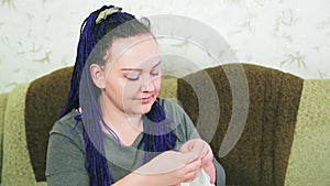 The blue-haired bride on the sofa sews her wedding dress by hand with a needle and thread