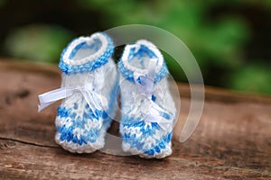 Blue hand made crochet baby booties on wooden background, closeup