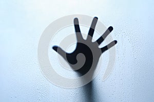 Blue hand silhouette behind a glass with water drops