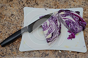 Blue-headed cabbage lying on a white chopping board with a large knife with a black handle