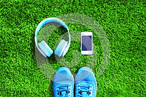 Blue a headphones and white smartphone with sports sneakers shoes on a green grass textured background, top view