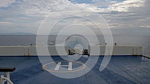 Blue helicopter landing pad on rear deck of ship sailing in calm seas