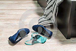 Blue high-heeled shoes, green-black lace thong panties and a condom on the wooden floor by the bed