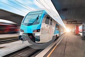 Blue high speed train in motion on the railway station at sunset