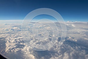 Blue horizon, view from the airplane`s porthole. Blue sky in the porthole, white fluffy clouds below.