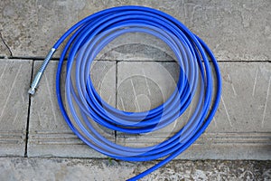 The blue hose of the spray gun is lying on the concrete