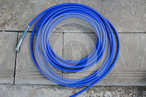 The blue hose of the spray gun is lying on the concrete