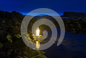 Blue hour at dark evening time, sea side, rocks and still water with a bright lantern in Sao Miguel, Azores.