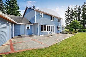 Blue house backyard with concrete floor patio area and well kept garden.