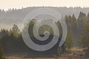 Blue house on a field in the middle of the misty forest at sunrise