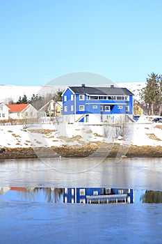 Blue house mirroring in the frozen fjord