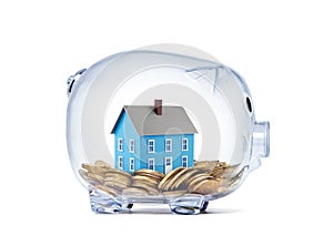 Blue house on money inside transparent piggy bank