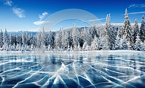 Blue ice and cracks on the surface of the ice. Frozen lake under a blue sky in the winter. The hills of pines. Winter