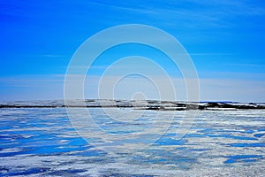 Blue ice and cracks on the surface of the ice. Frozen lake under a blue sky in the winter.