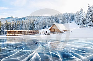 Blue ice and cracks on the surface of the ice. Frozen lake under a blue sky in the winter. Cabin in the mountains