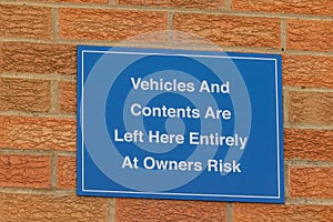 Blue information sign,Vehicles and contents are left here entirely at owners risk, on red brick wall