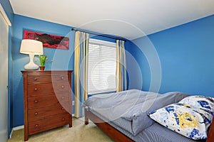 Blue interior of a small bedroom with brown dresser