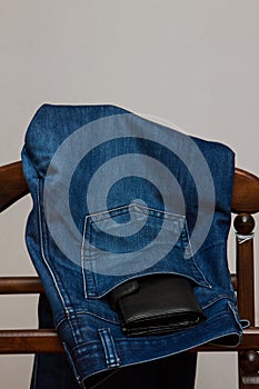 Blue jeans with a black purse hanging on a wooden hanger