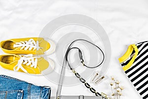 Blue jeans and jacket, bag and yellow sneakers on white bed. Women`s stylish summer or spring outfit. Trendy fashion clothes.