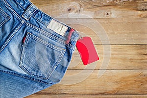 Blue jeans with red blank tag on wooden background