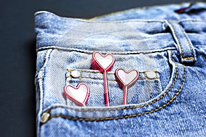 Blue jeans and red hearts from pocket on black background top view flat lay. Detail of nice blue jeans. Jeans texture or denim