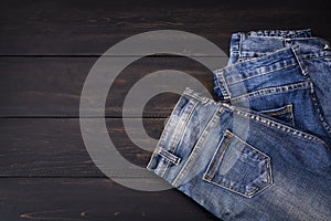 Blue jeans resting on a dark black wooden table. Modern fashion jeans - top view with space to copy text