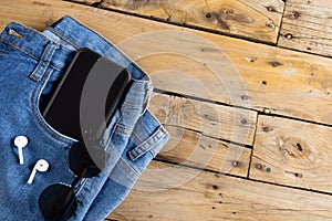 Blue jeans with smartphone, earphones and glasses lying on wooden surface