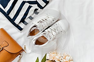 Blue jeans, t shirt, bag and white sneakers on white bed. Trendy clothes. Women`s casual spring summer outfit. Fashion concept.