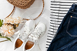 Blue jeans, t shirt, bag and white sneakers on white bed. Trendy clothes. Women`s casual spring summer outfit. Fashion concept.