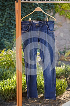 Blue jeans weigh on wooden hanger in yard