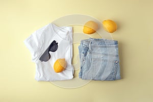 Blue jeans, white shirt, sunglasses and lemons on yellow background. Women`s stylish spring summer outfit. Trendy clothes. Flat