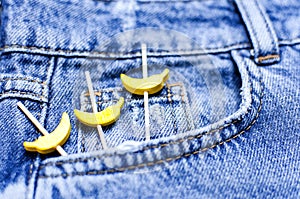 Blue jeans and yellow wooden bananas from a pocket on black background top view flat lay. Detail of nice blue jeans. Jeans texture