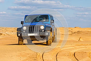 Blue Jeep Wrangler Rubicon Unlimited at desert sand dunes