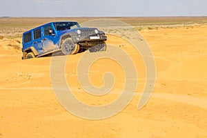 Blue Jeep Wrangler Rubicon Unlimited at desert sand dunes