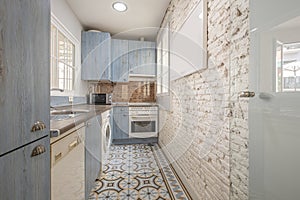 Blue kitchen cabinets with wood grain and white appliances, an exposed white brick wall and hydraulic tile floor