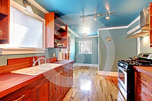 Blue kitchen with cherry cabinets and shiny floor.