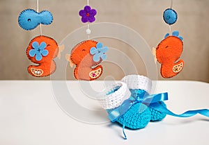 Blue knitted baby shoes with a blue ribbon around toys rattles.