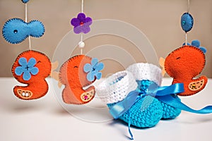 Blue knitted baby shoes with a blue ribbon around toys rattles.