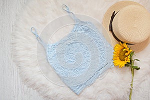 Blue lace top, straw hat and sunflower. On white fur, top view