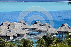 Blue lagoon of the Bora Bora island, Polynesia. Top view on palm trees, traditional lodges over water and the sea