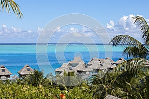 Blue lagoon of the Bora Bora island, Polynesia. Top view on palm trees, traditional lodges over water and the sea