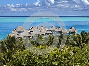 Blue lagoon of the Bora Bora island, Polynesia. Top view on palm trees, traditional lodges over water and the sea