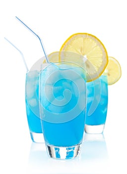 Blue lagoon cocktails with ice cubes, lemon and straw on white