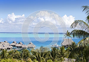 Blue lagoon of the island of Bora Bora, Polynesia. A view from height on palm trees, traditional lodges over water and the sea