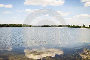 The blue lake reflects the sky and clouds. It s a sunny summer day.