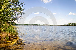 The blue lake reflects the sky and clouds. It s a sunny summer day.