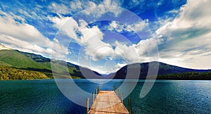 Blue lake with wooden pier surrounded with mountains in New Zealand