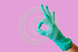 Blue latex medical gloves on a female hand, shows the character is good on a light pink background. The concept of medicine and
