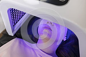 Blue led light mask for face skin therapy, care. Young girl gets problem skin treatment